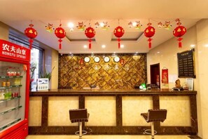 A hotel reception area with a marble counter, two bar stools, a red sign, and decorative lanterns.