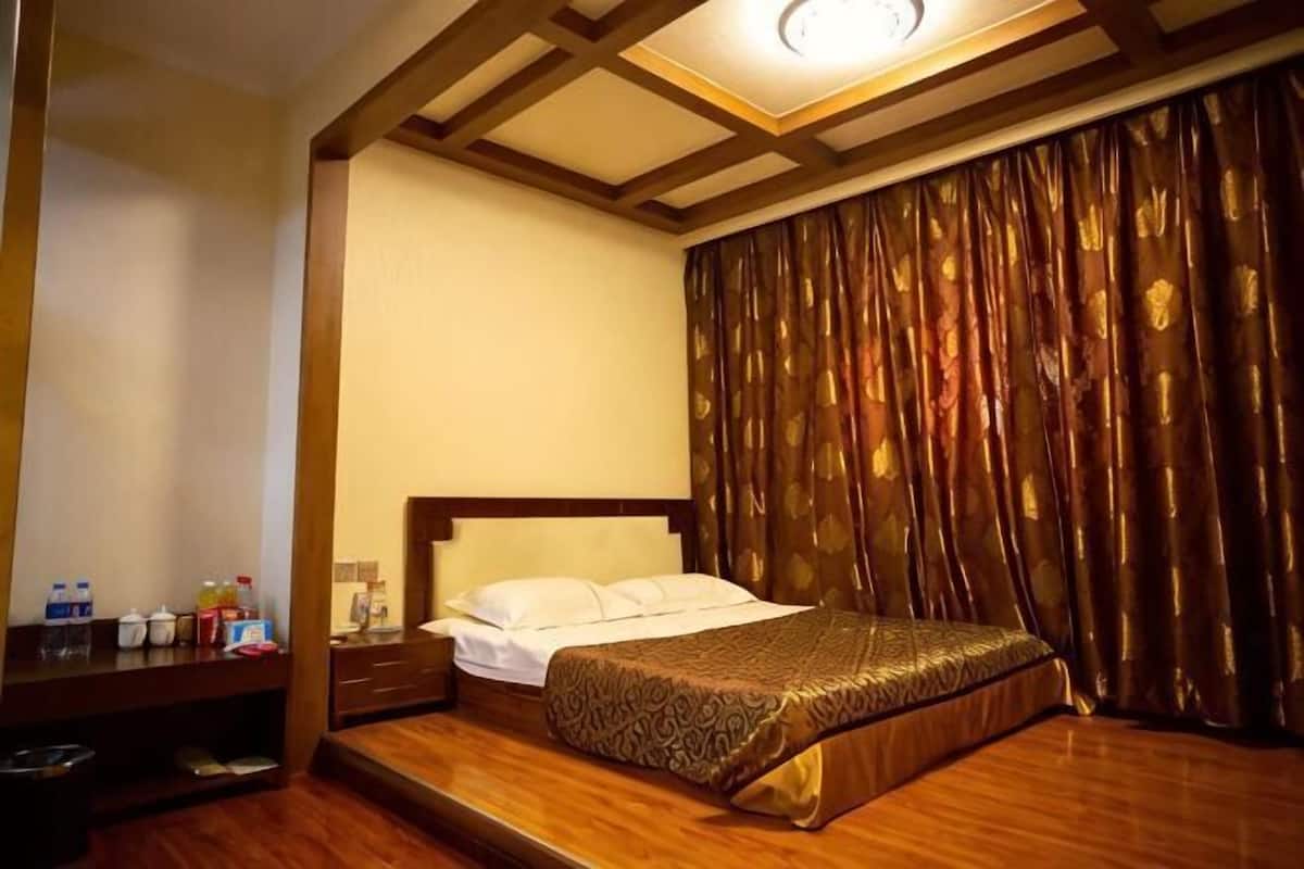 A hotel room with a bed, wooden headboard, curtains, and a nightstand with toiletries.