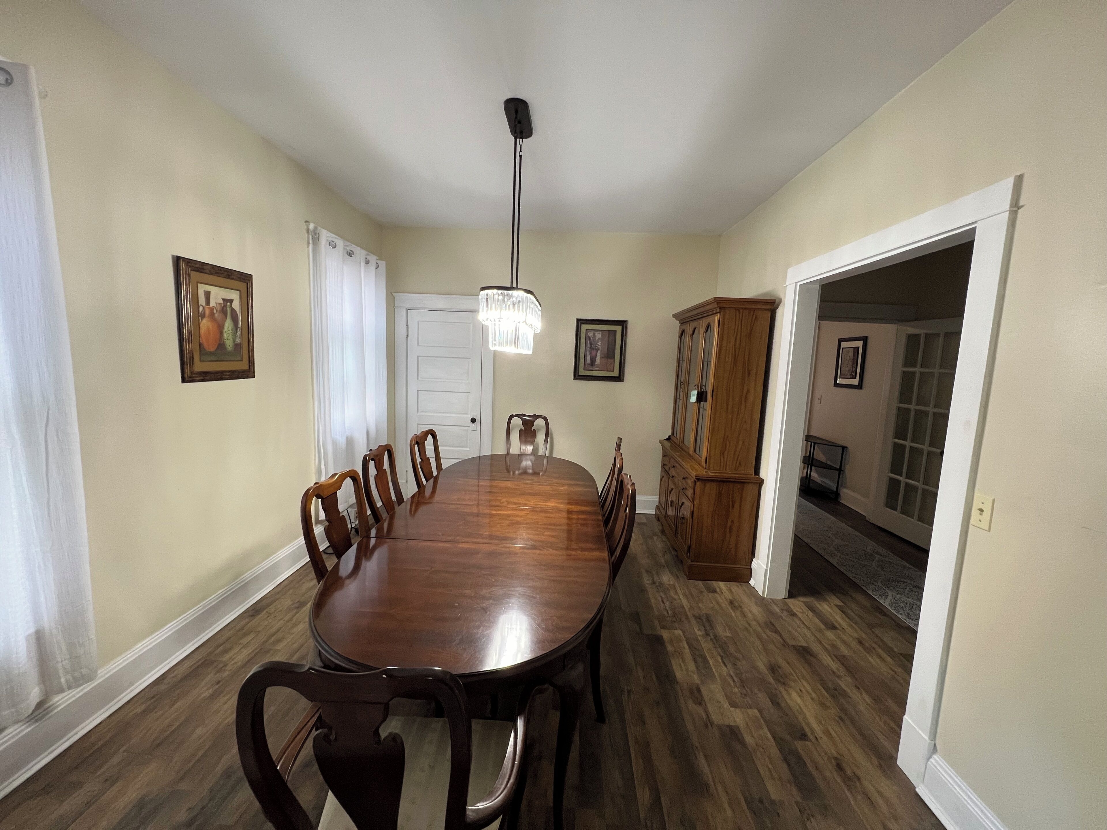 A dining room with a wooden table and chairs, a chandelier, and a wooden cabinet.