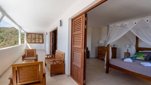 A balcony with wooden furniture, a bed with a canopy, and a view of the outdoors. - Villa Malinina, swimming pool, sea view (Les Anses-d'Arlet.)