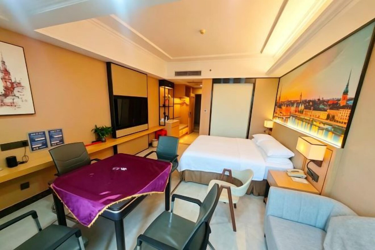 A hotel room with a bed, a desk with a computer, a TV, and a cityscape painting.