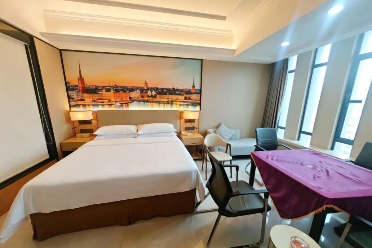 Quarto de hotel com uma cama grande, uma escrivaninha, uma cadeira e vista para a paisagem urbana.