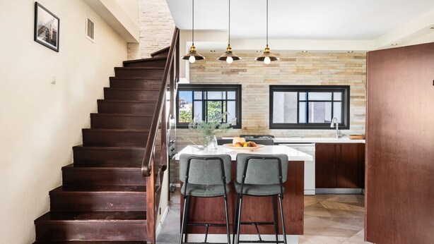 A modern kitchen with a central island, bar stools, and a staircase leading to an upper level. - Hasharon Rooftop Oasis by Sea N' Rent (Ramat Hasharon)