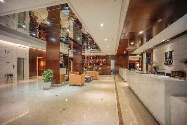 A spacious lobby with a reception desk, seating area, and a large bookshelf. - Qixin Hotel (Hangzhou)