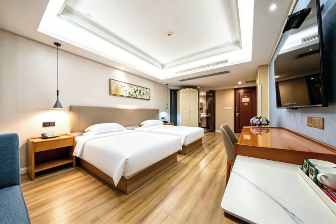 A hotel room with two beds, a desk, a TV, and a ceiling light.