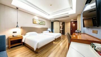 A hotel room with two beds, a desk, a TV, and a ceiling light.