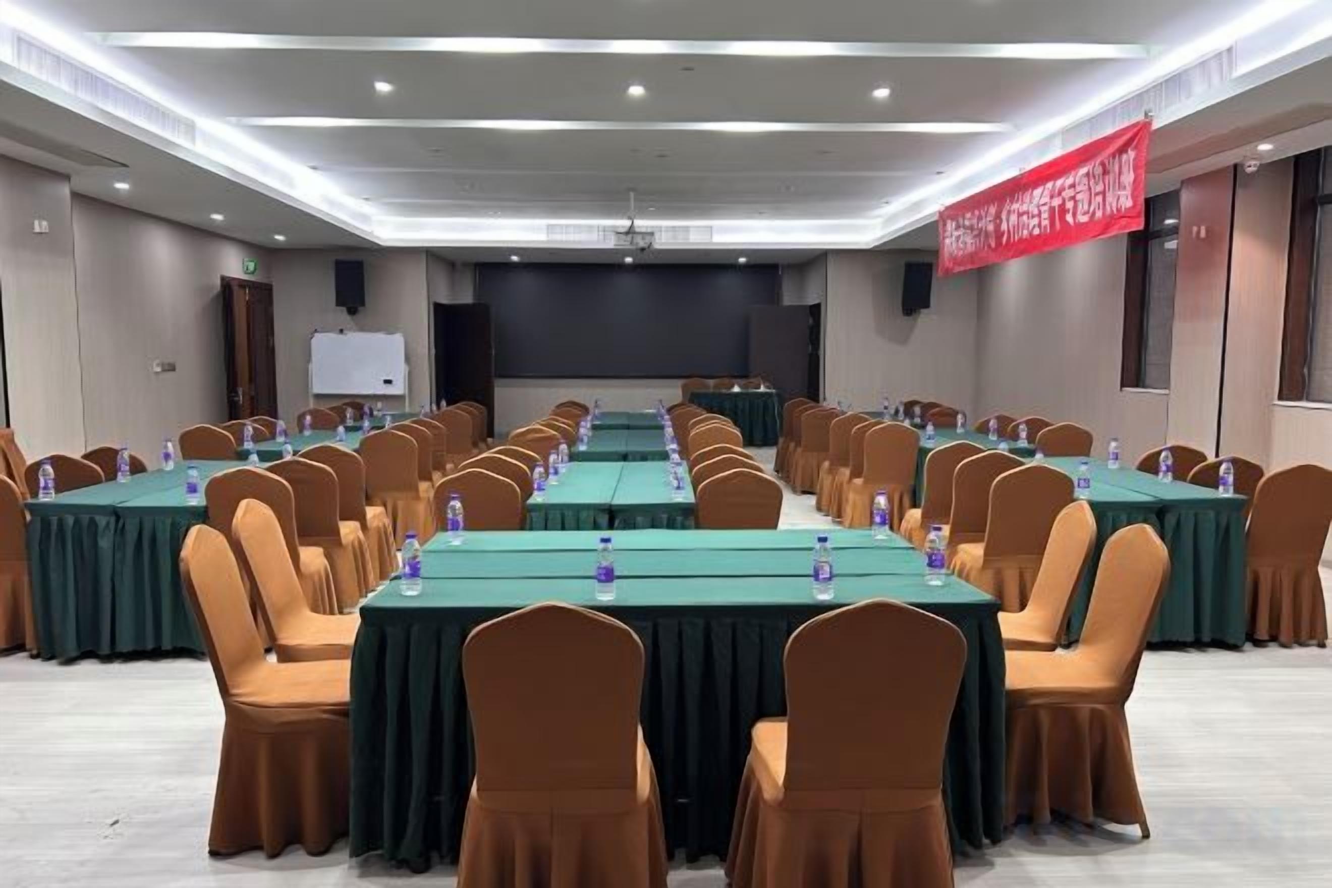 A conference room with rows of tables and chairs, a projector screen, and a red banner.