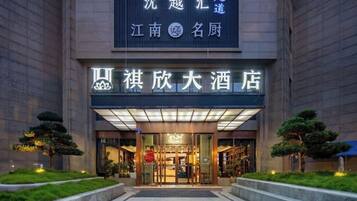 A hotel entrance with a sign above the door, a well-lit facade, and a landscaped area with trees.