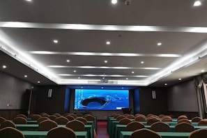 A conference room with rows of chairs, a large screen, and a projector. - Qixin Hotel (Hangzhou)