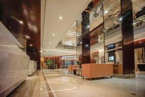 A modern hotel lobby with a reception desk, seating area, and a large mirror reflecting the space. - Qixin Hotel (Hangzhou)