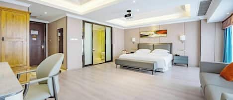 Ett modernt hotellrum med en säng, ett skrivbord, en stol, en soffa och en skjutdörr som leder till ett badrum.