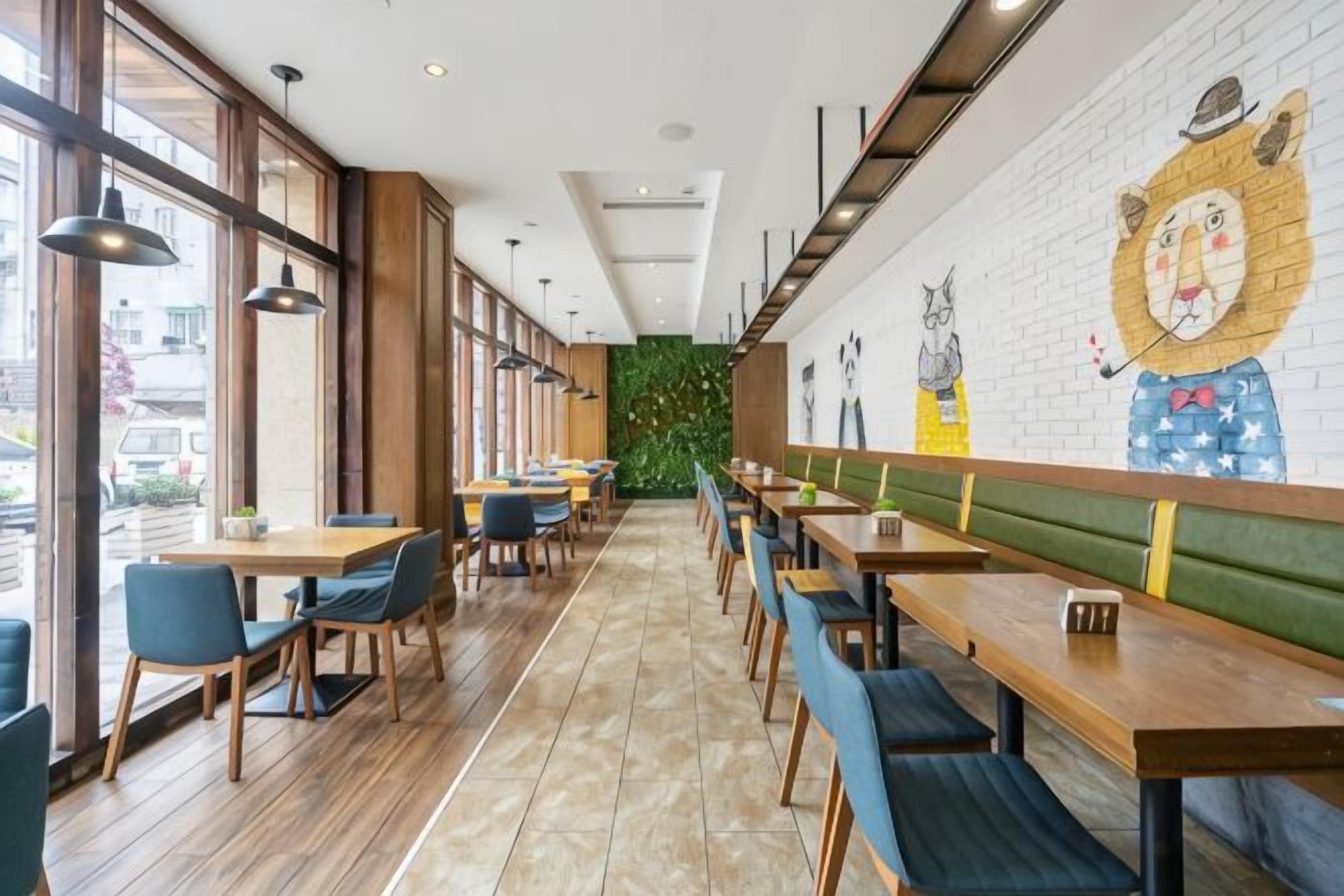 A restaurant with long tables and booths, a mural on the wall, and large windows.