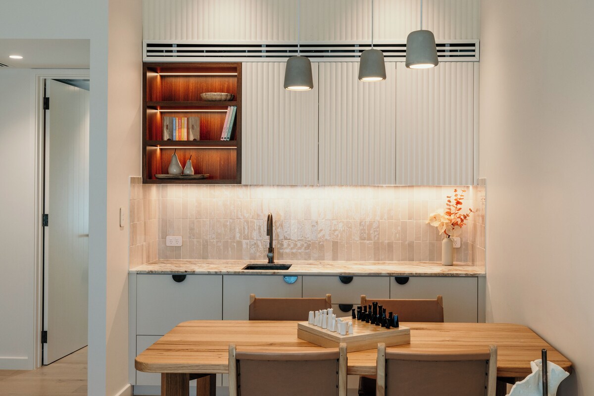 Una cucina moderna con un tavolo da pranzo in legno, lampade a sospensione e una libreria a muro.