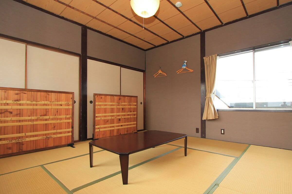 A tatami mat room with a low table, wooden sliding doors, and a window with curtains.