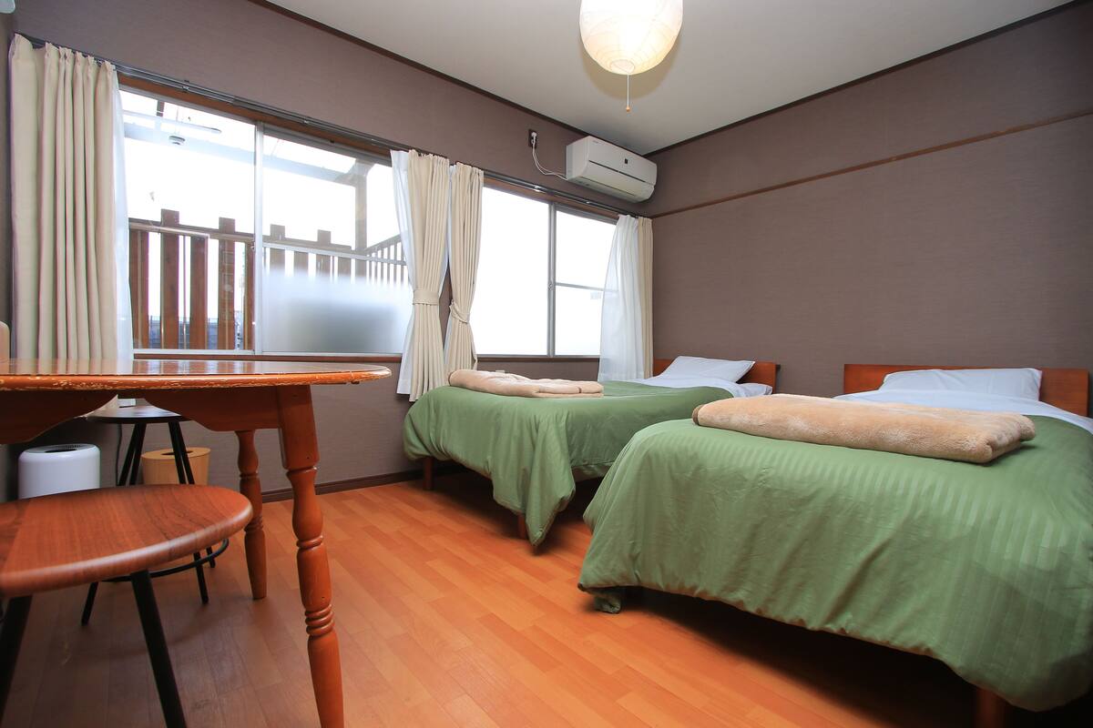 A room with two beds, a wooden table, and a chair.