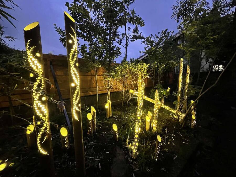 Un jardín con estructuras e iluminación y plantas al anochecer.
