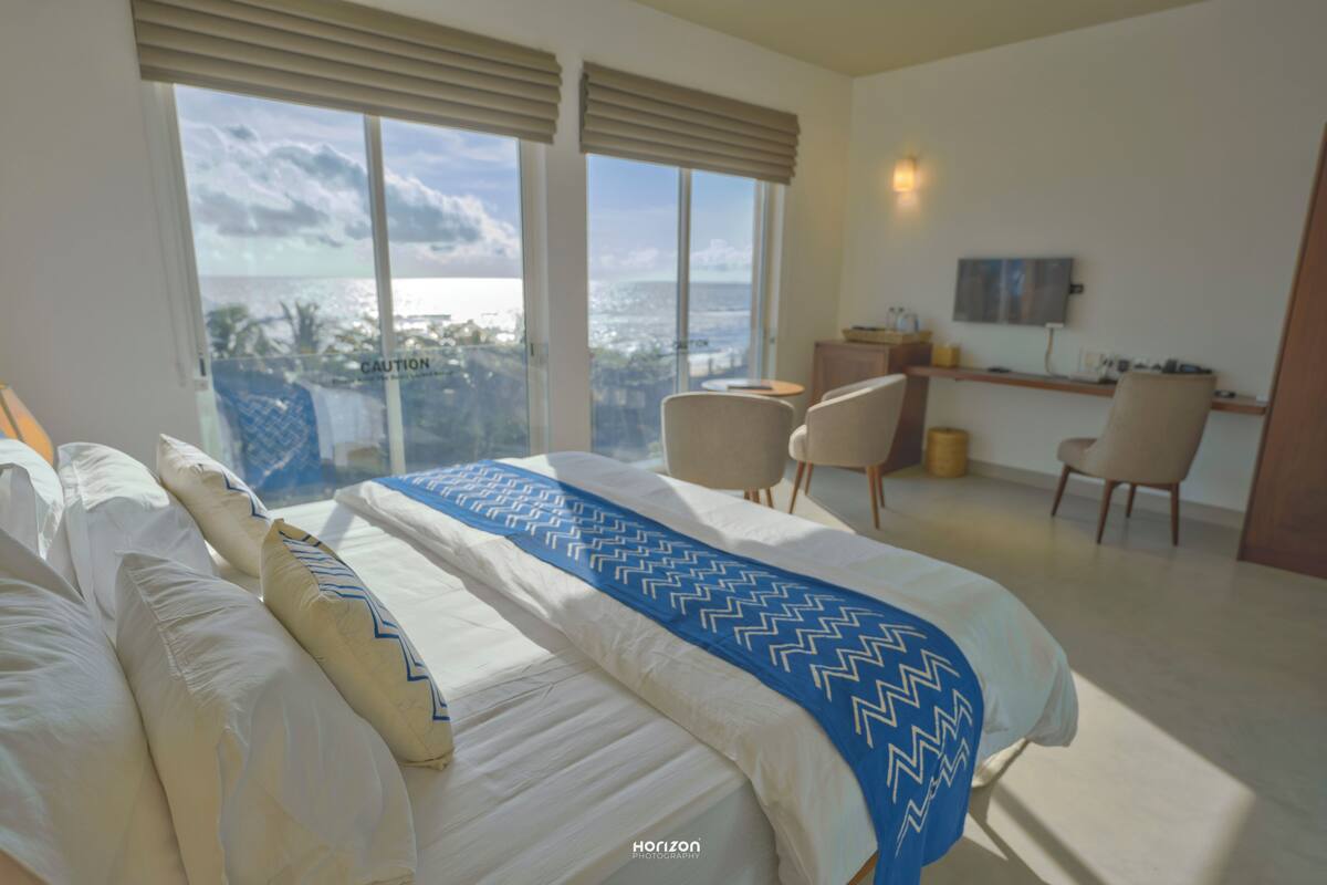 A hotel room with a large bed, two chairs, a desk, and a view of the city.
