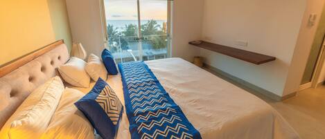 A bedroom with a bed, pillows, a bedside table, a window with a view, and a shelf.
