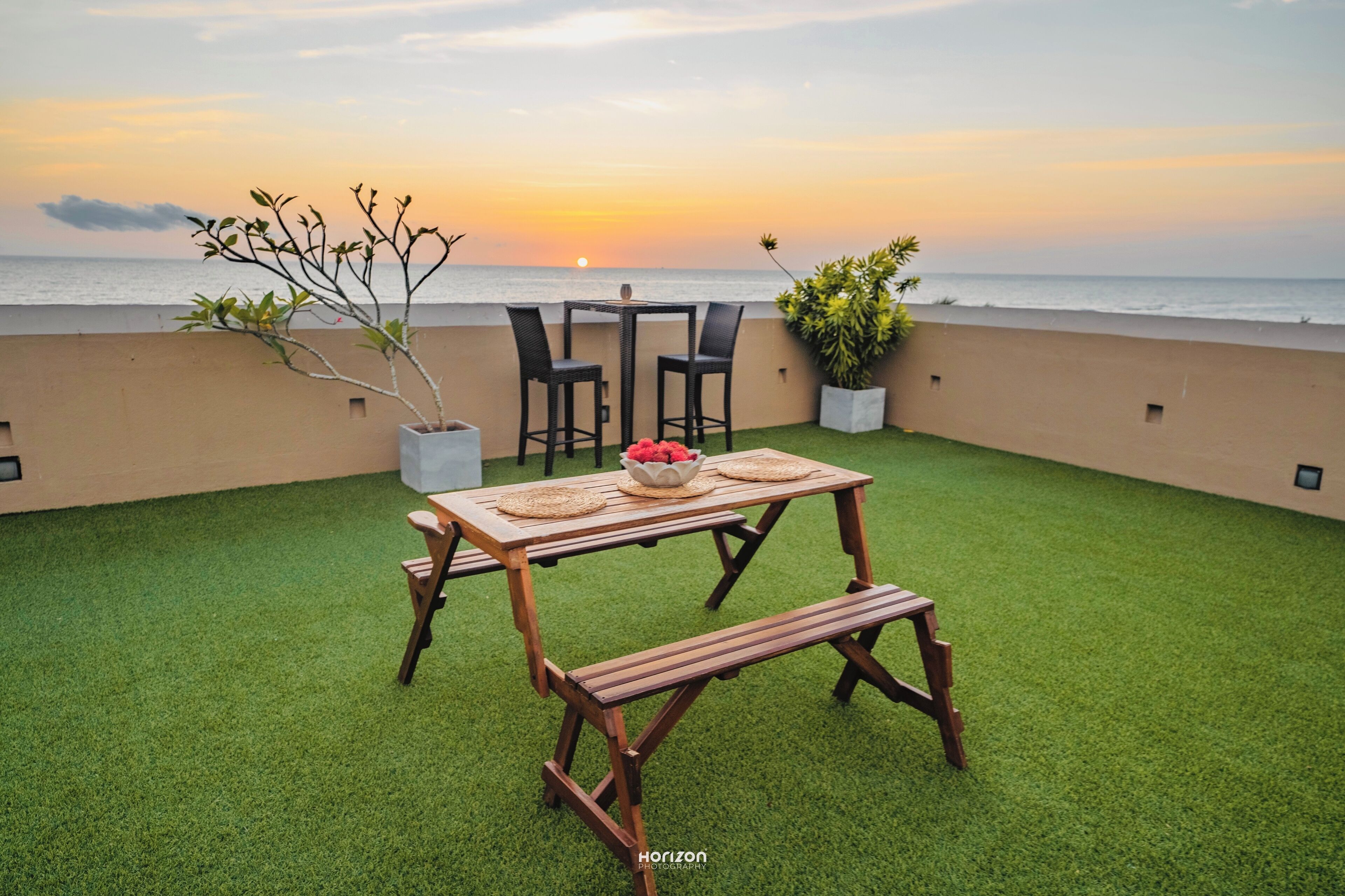 Una terraza con mesa y sillas de madera, un banco y plantas en macetas.