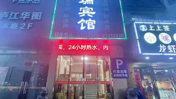A hotel entrance with a neon sign, a visible reception desk, and a parking sign.