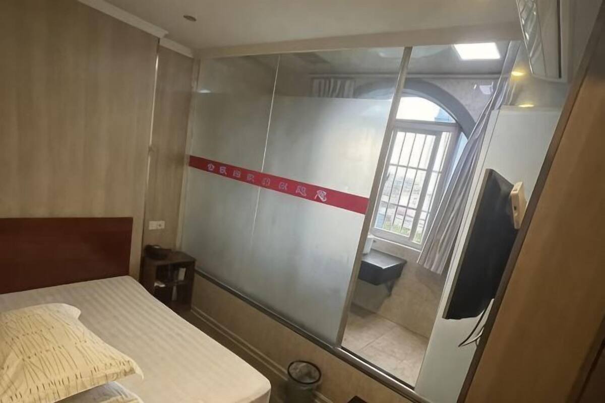 A bedroom with a bed, a wardrobe, a small table, and a window with a view.
