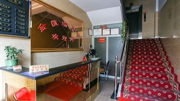 A hotel reception area with a reception desk, a red carpeted staircase, and a wall-mounted sign with Chinese characters.