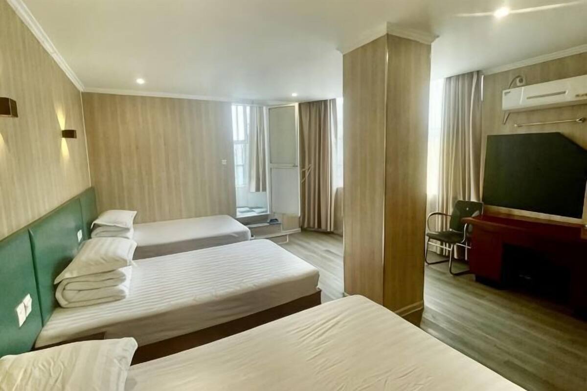 A hotel room with two beds, a TV, a desk, and a window.