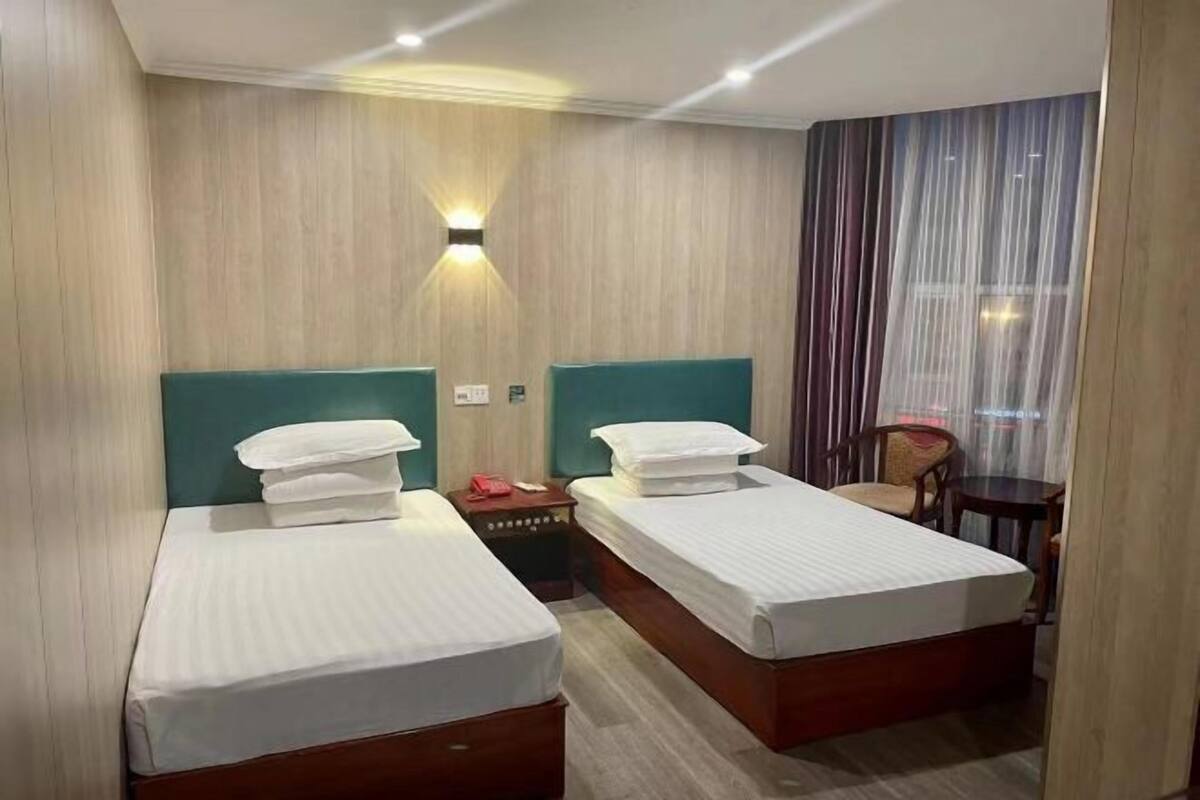 A hotel room with two beds, a nightstand, a chair, and a window with curtains.
