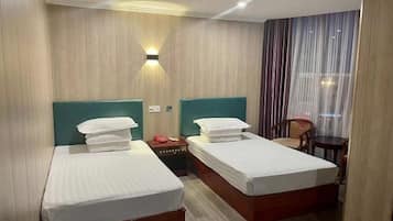 A hotel room with two beds, a nightstand, a chair, and a window with curtains.