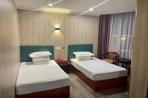 Hotellihuone, jossa on kaksi sänkyä, yöpöytä, tuoli ja ikkuna, jossa on verhot.