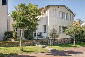 A two-story building with a flat roof, a front entrance with steps, and a small patio area with outdoor seating. - Ferienwohnung Astrid - Moderne Parterre-ferienwohnung mit Terrasse, nah am Strand (Heringsdorf)