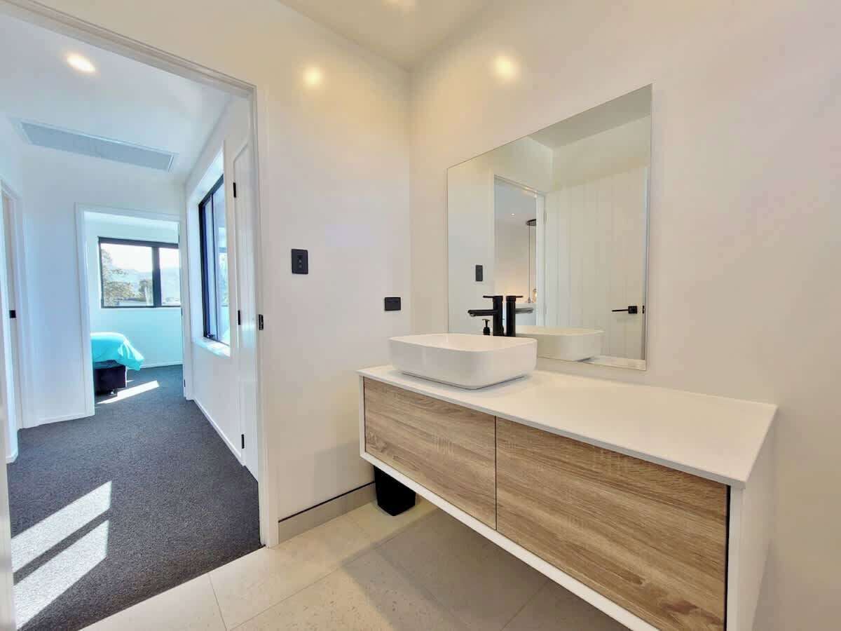 A modern bathroom with a white vanity, a large mirror, and a view into the adjacent bedroom.