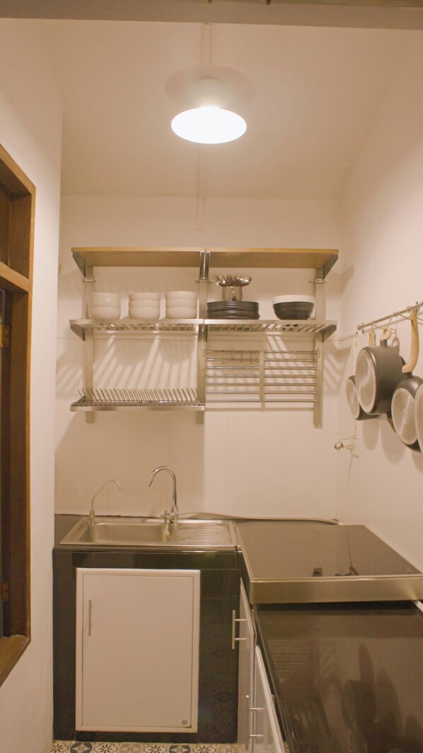 Una cocina compacta con un lavamanos, estufa y estantes superiores con vajilla y utensilios de cocina.