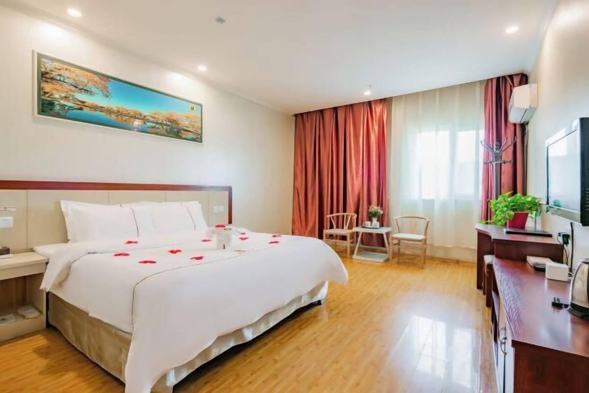 A hotel room with a bed, a desk, a chair, a TV, and a painting on the wall.