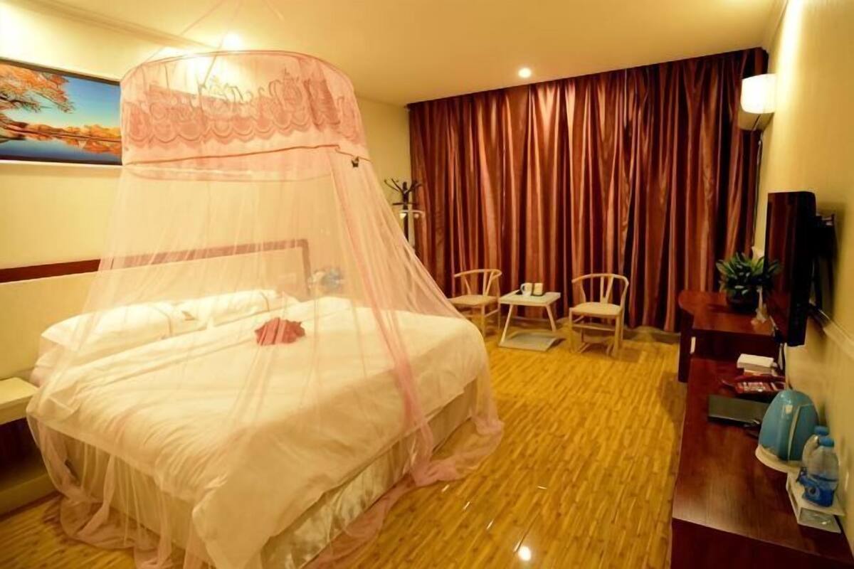A hotel room with a bed, a desk, a chair, a TV, and a curtain.