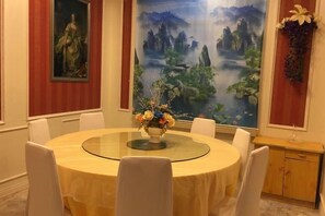 A round dining table with a glass top, surrounded by white chairs, in a room with red walls and a large landscape painting. - Super 8 Hotel (Korla Tianshan West Road) (Korla)