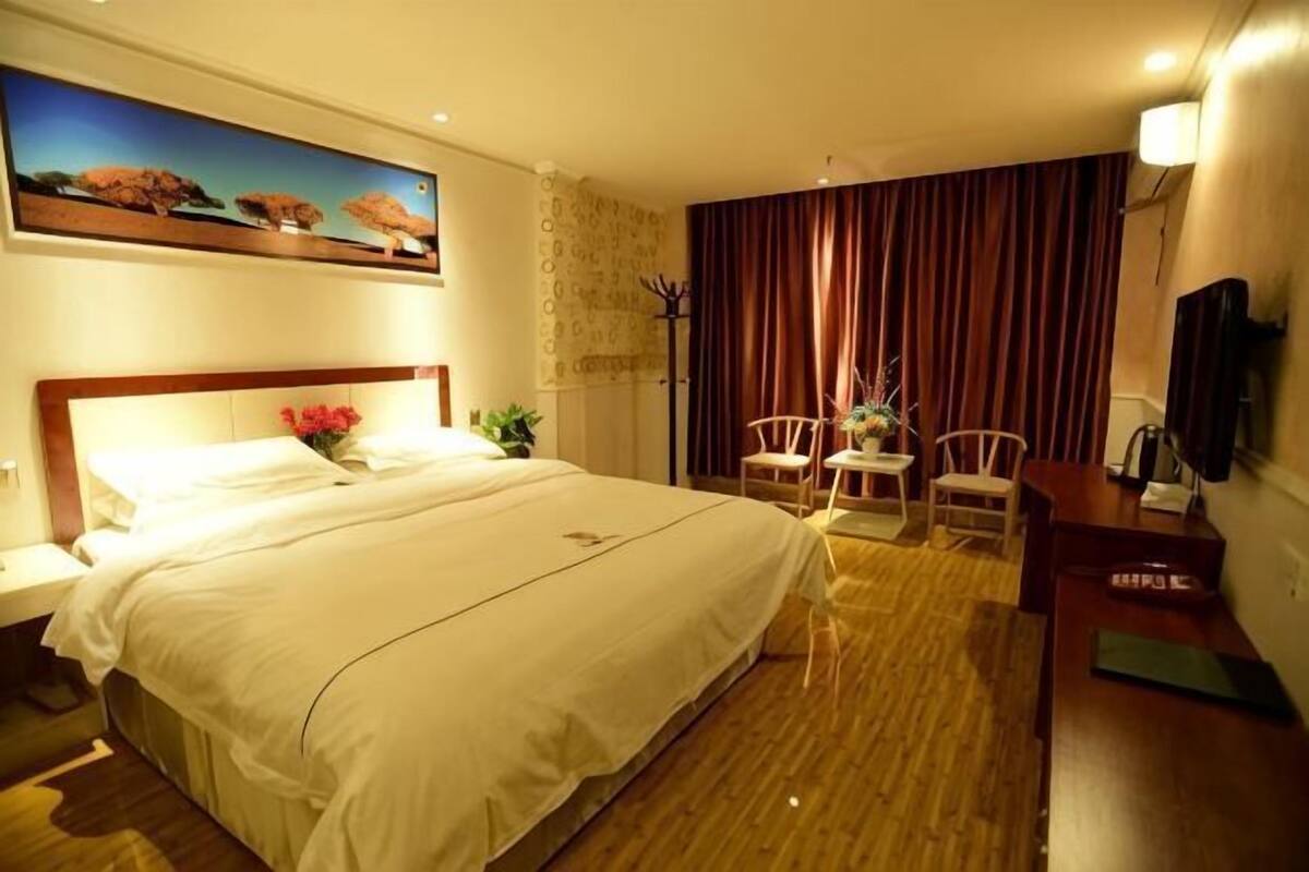 A hotel room with a large bed, a desk, a chair, a television, and a painting on the wall.