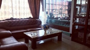 Un salon avec un canapé en cuir marron, une table basse en marbre et une porte en verre donnant sur un balcon où se trouve un vélo.
