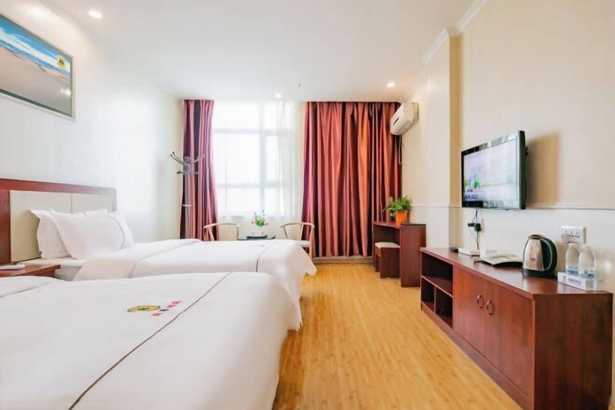 A hotel room with two beds, a desk, a TV, and a window with curtains.