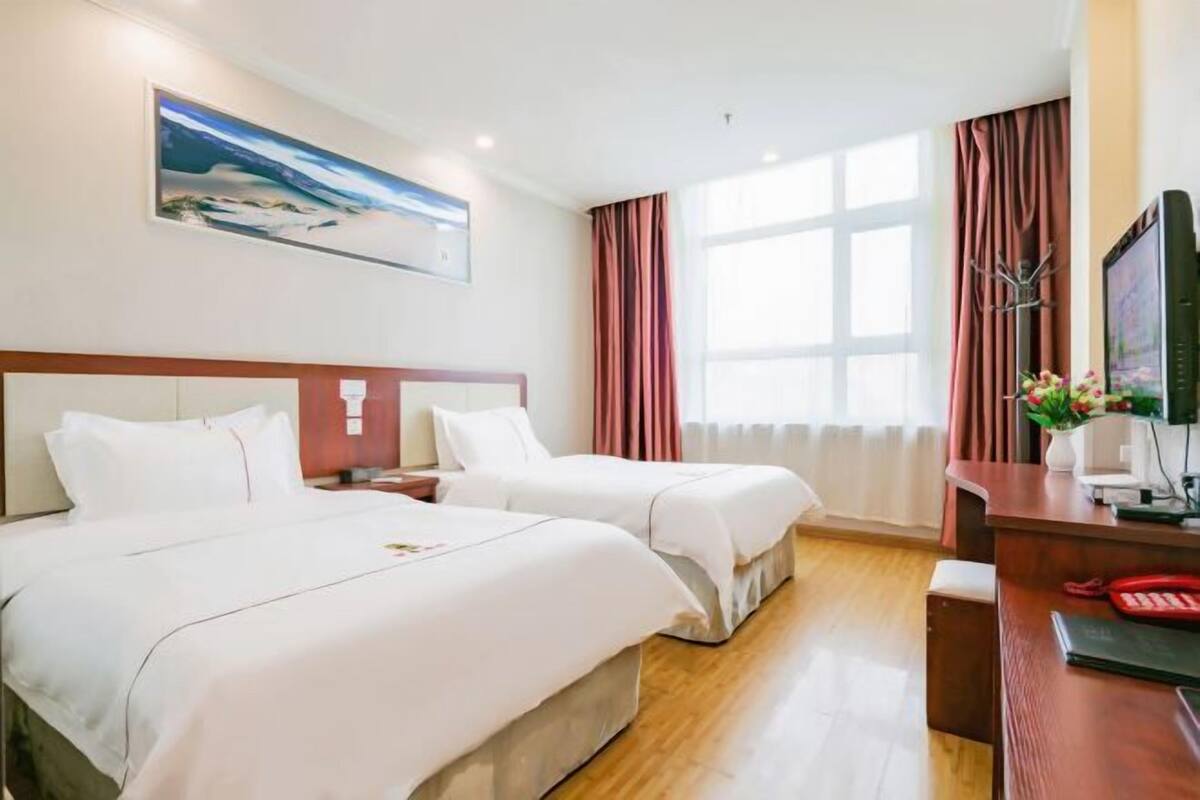 A hotel room with two beds, a desk with a computer, a TV, and a painting on the wall.