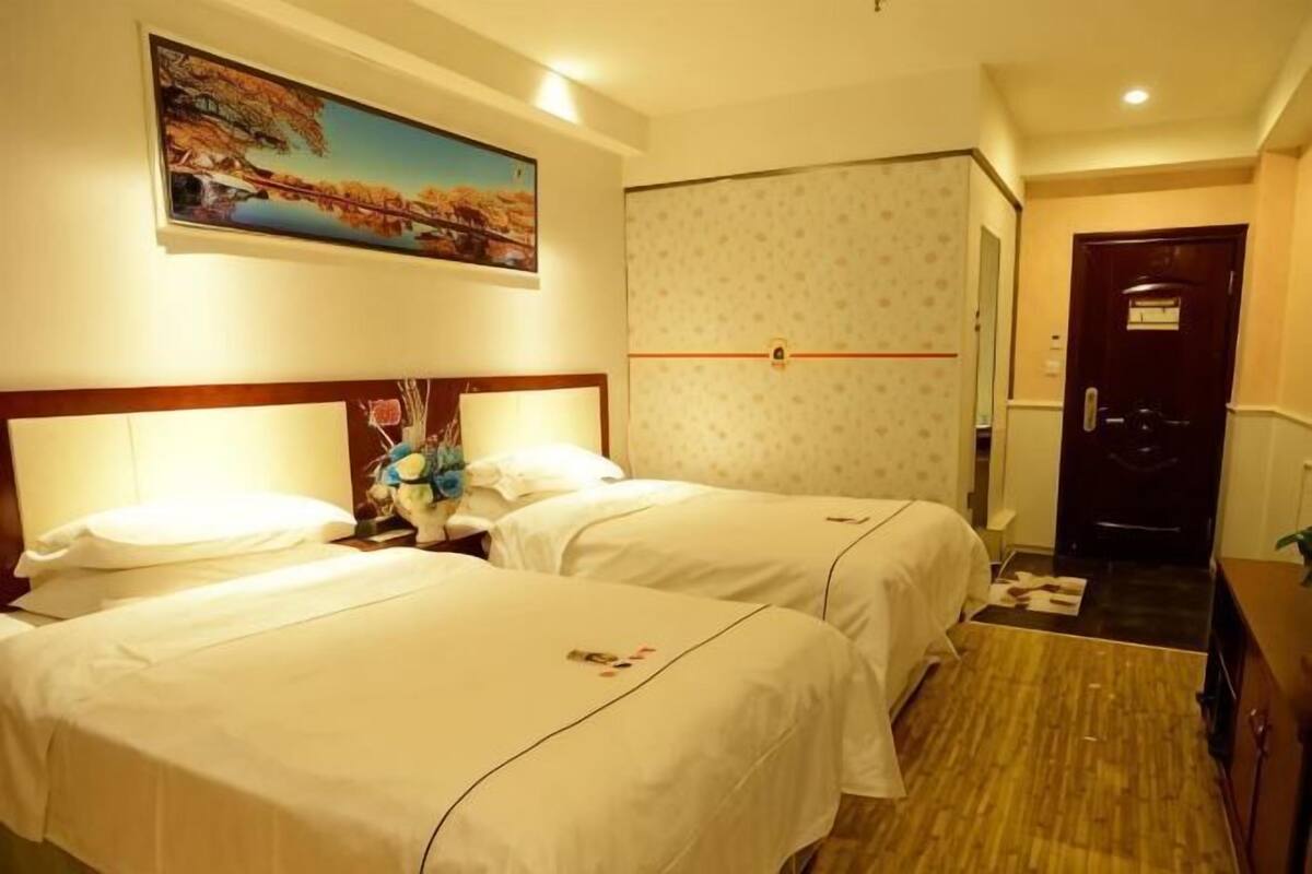A hotel room with two beds, a painting on the wall, a door, and a small desk.