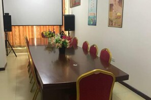 A conference room with a long table, red chairs, a floral centerpiece, and a projector screen. - Super 8 Hotel (Korla Tianshan West Road) (Korla)