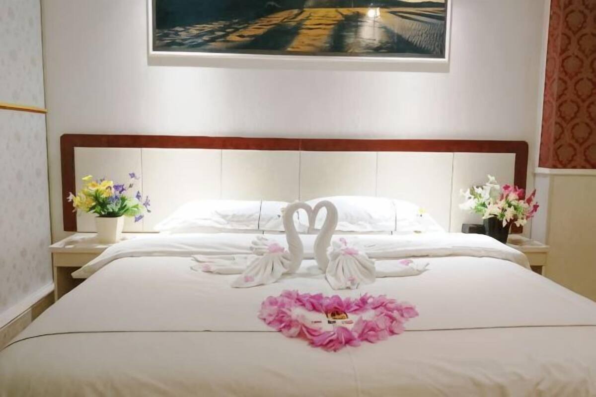 A hotel room with a neatly made bed, a painting above the bed, and two nightstands with floral arrangements.