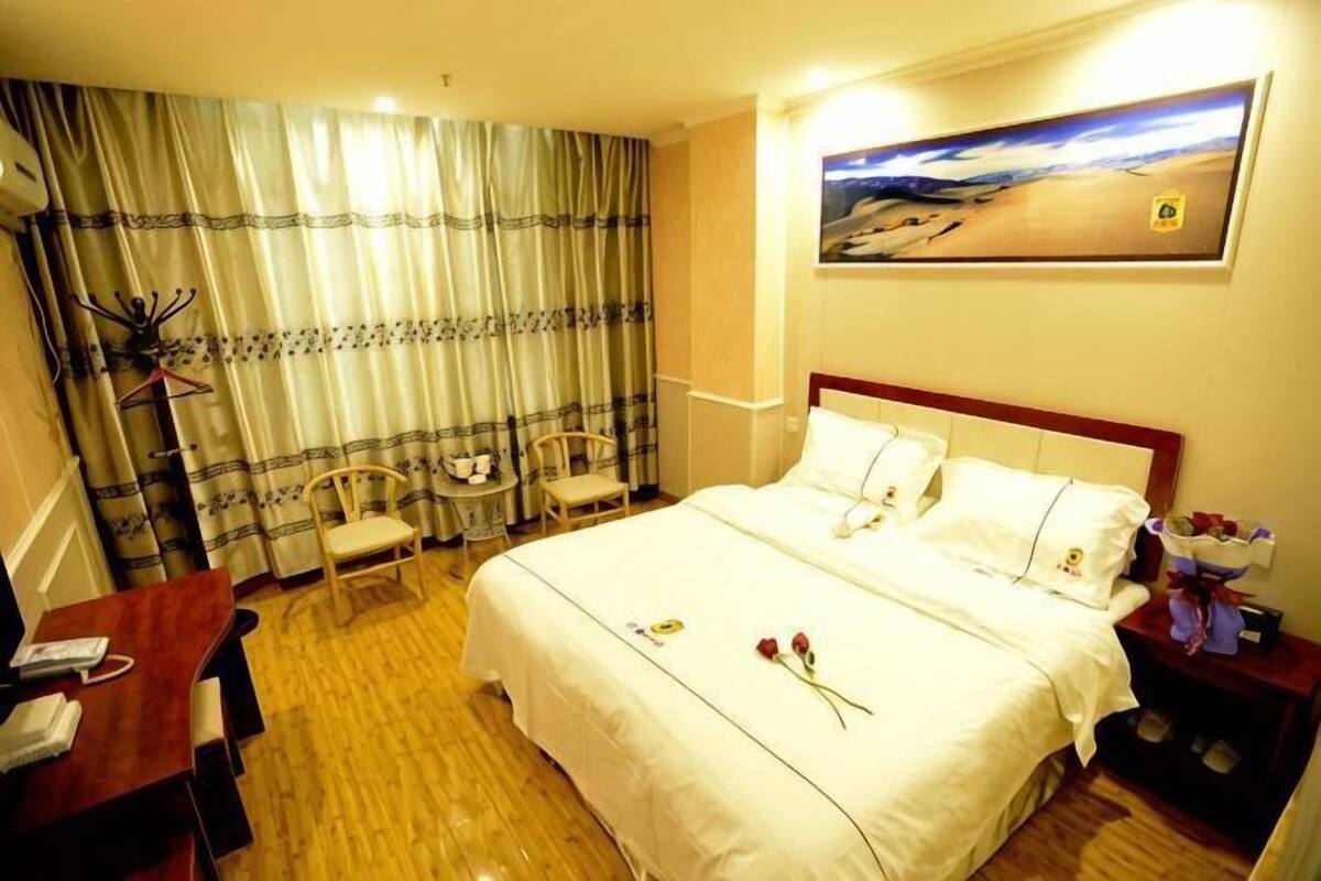 A hotel room with a large bed, a desk, two chairs, a nightstand, and a painting on the wall.