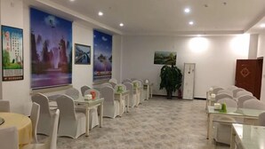 Une salle de conférence avec des chaises et des tables blanches, une grande plante et des œuvres d’art accrochées aux murs.