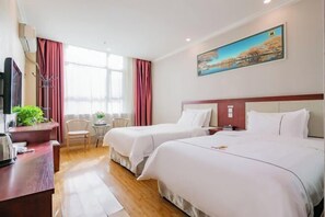 Une chambre d’hôtel avec deux lits, un bureau agrémenté d’une plante, une télévision et un tableau au mur.