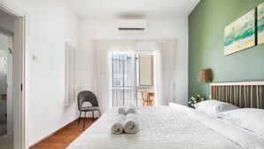 A hotel room with a large bed, a chair, a window with curtains, and a green wall with artwork. - Ben Yehuda Green Charm by Sea N' Rent (Tel Aviv)