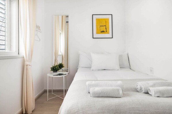 A hotel room with a bed, a bedside table with a plant, a mirror, and a framed picture on the wall. - Ben Yehuda Green Charm by Sea N' Rent (Tel Aviv)