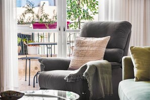 A modern living room with a grey sofa, a knitted throw pillow, and a view of a balcony with plants. - Ben Yehuda Green Charm by Sea N' Rent (Tel Aviv)