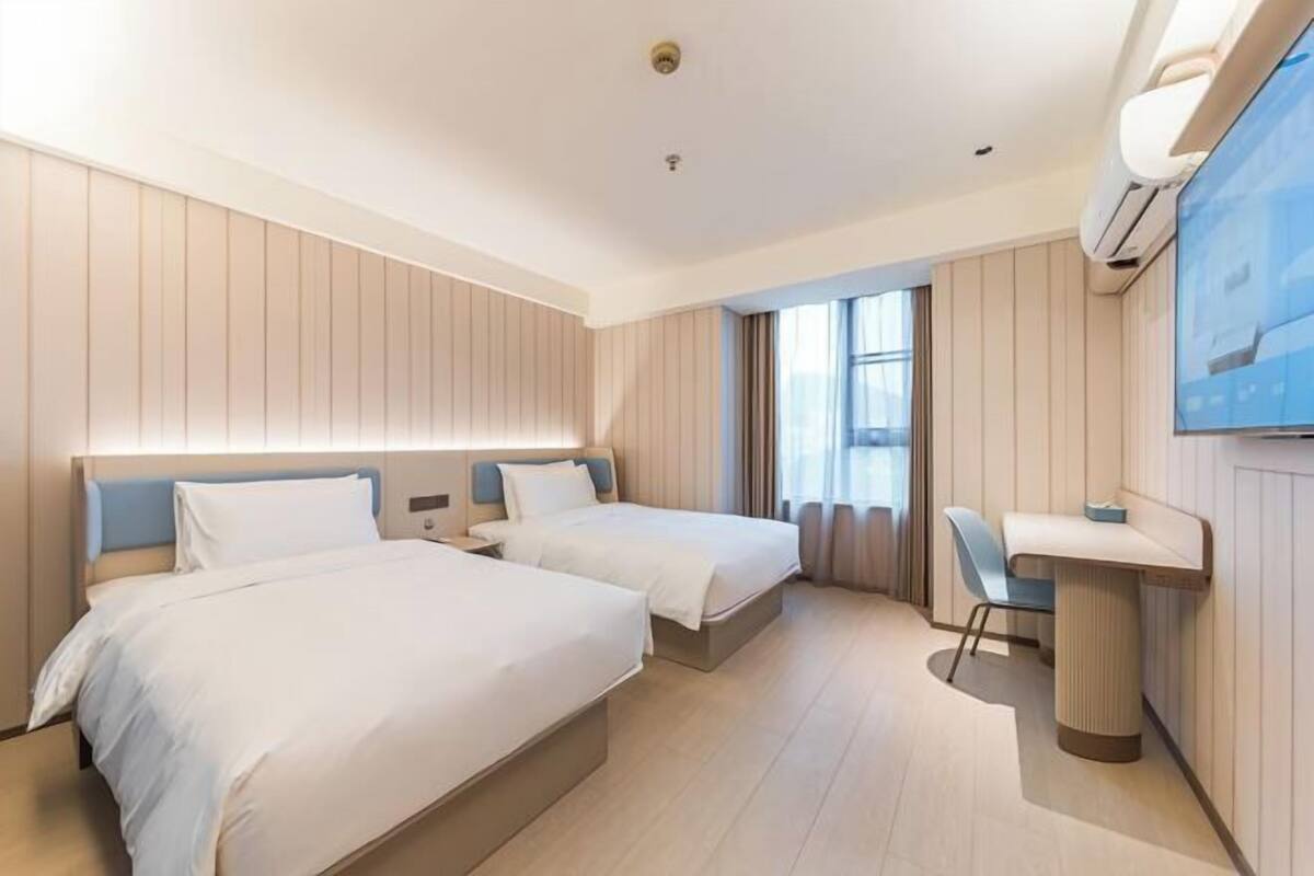 A hotel room with two beds, a desk, and a TV.